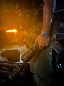 SWCS tactical watch beside rifle and patrol vehicle at night